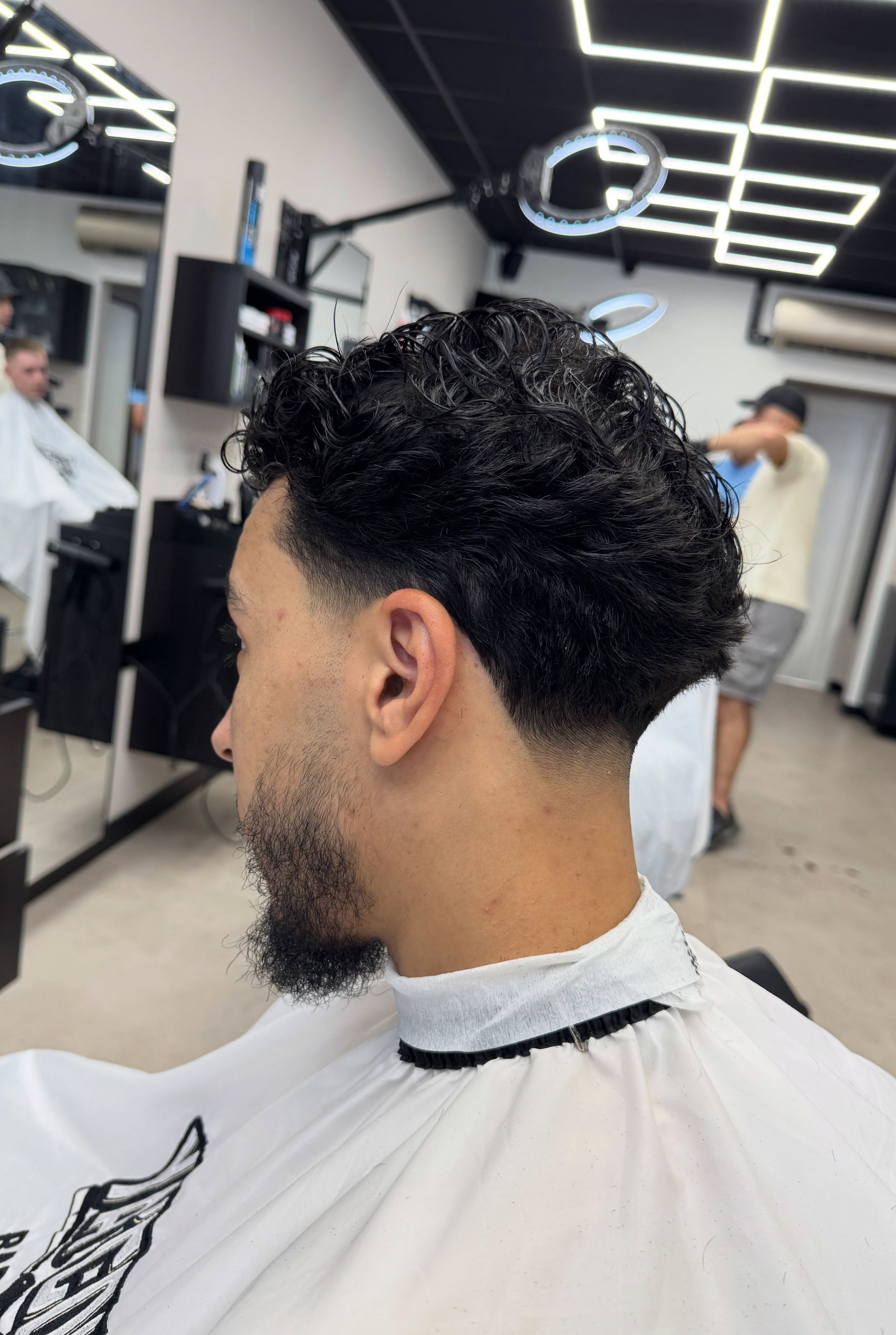 Krullen bovenop met een lage taper en een strak bijgewerkte baard